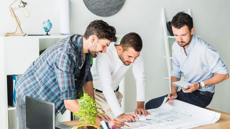 Three men at desk looking at blueprints illustrate blog "Project Managers and Stakeholder Cooperation: What You Need To Know"
