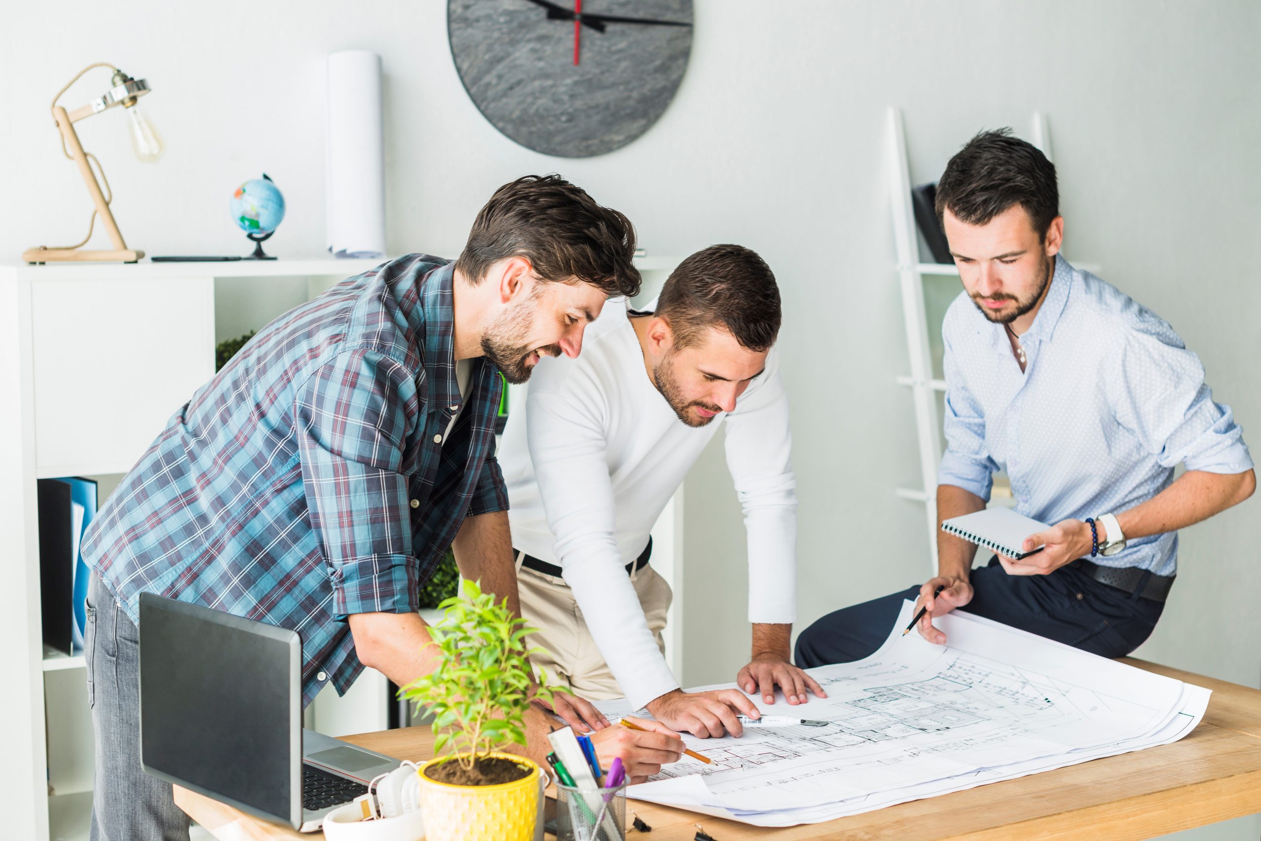 Three men at desk looking at blueprints illustrate blog "Project Managers and Stakeholder Cooperation: What You Need To Know"