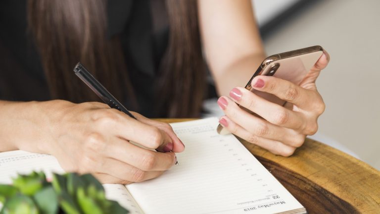 Closeup of woman taking notes illustrates blog "Do Project Managers Take Meeting Minutes?"
