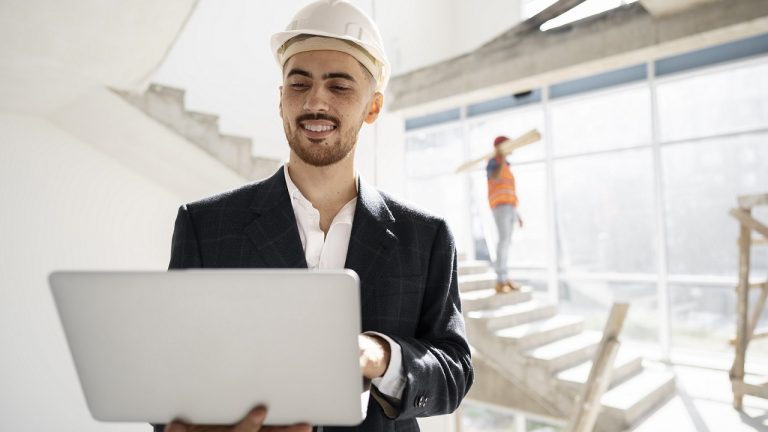 Man with hard hat and laptop illustrates blog "Project manager vs construction manager: What Is the Difference?"